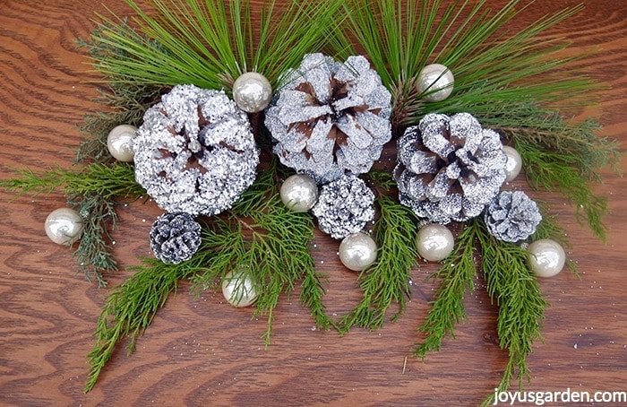 A-decoration-of-silver-painted-glittered-pine-cones-with-pearlescent-balls-fresh-evergreen-branches-sit-on-a-table.-Shimmery-silver-cone-DIY_new.jpg